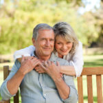 Senior woman hugging her husband who is on the bench
