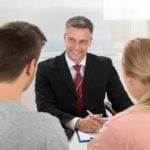 Mature Happy Estate Agent Talking To Young Couple In Office
